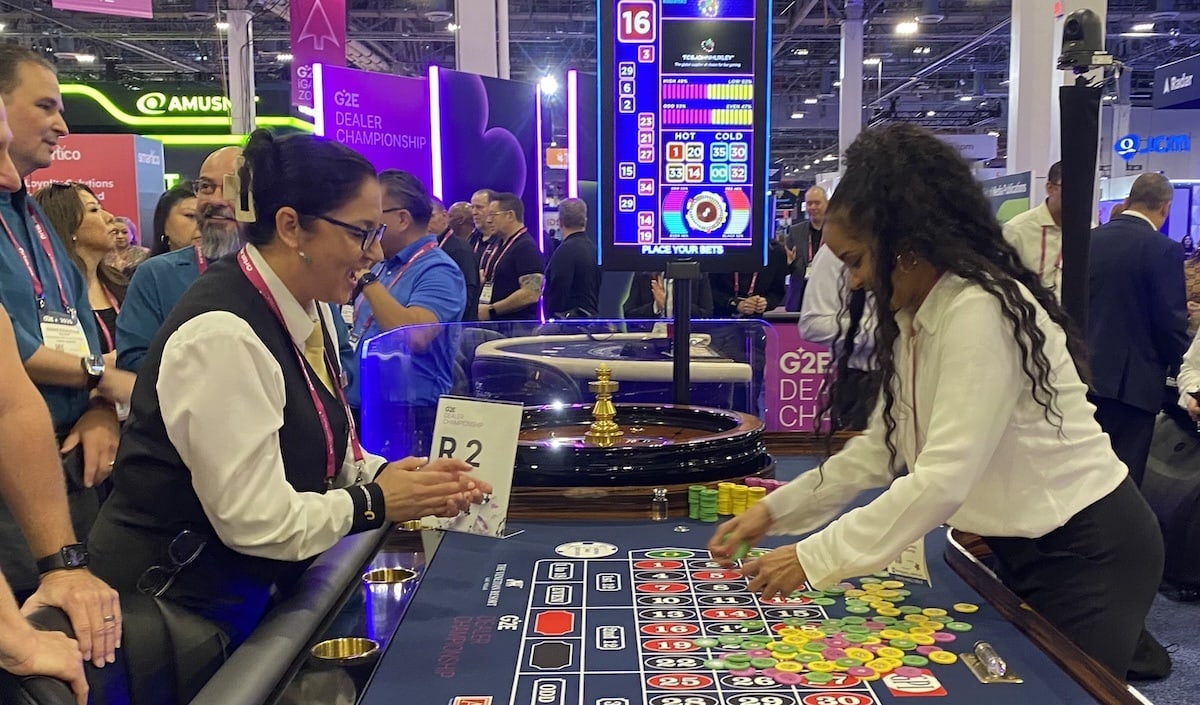 Horseshoe Casino table games dealer encourages Downtown Grand casino dealer in G2E's cheque racking competition.