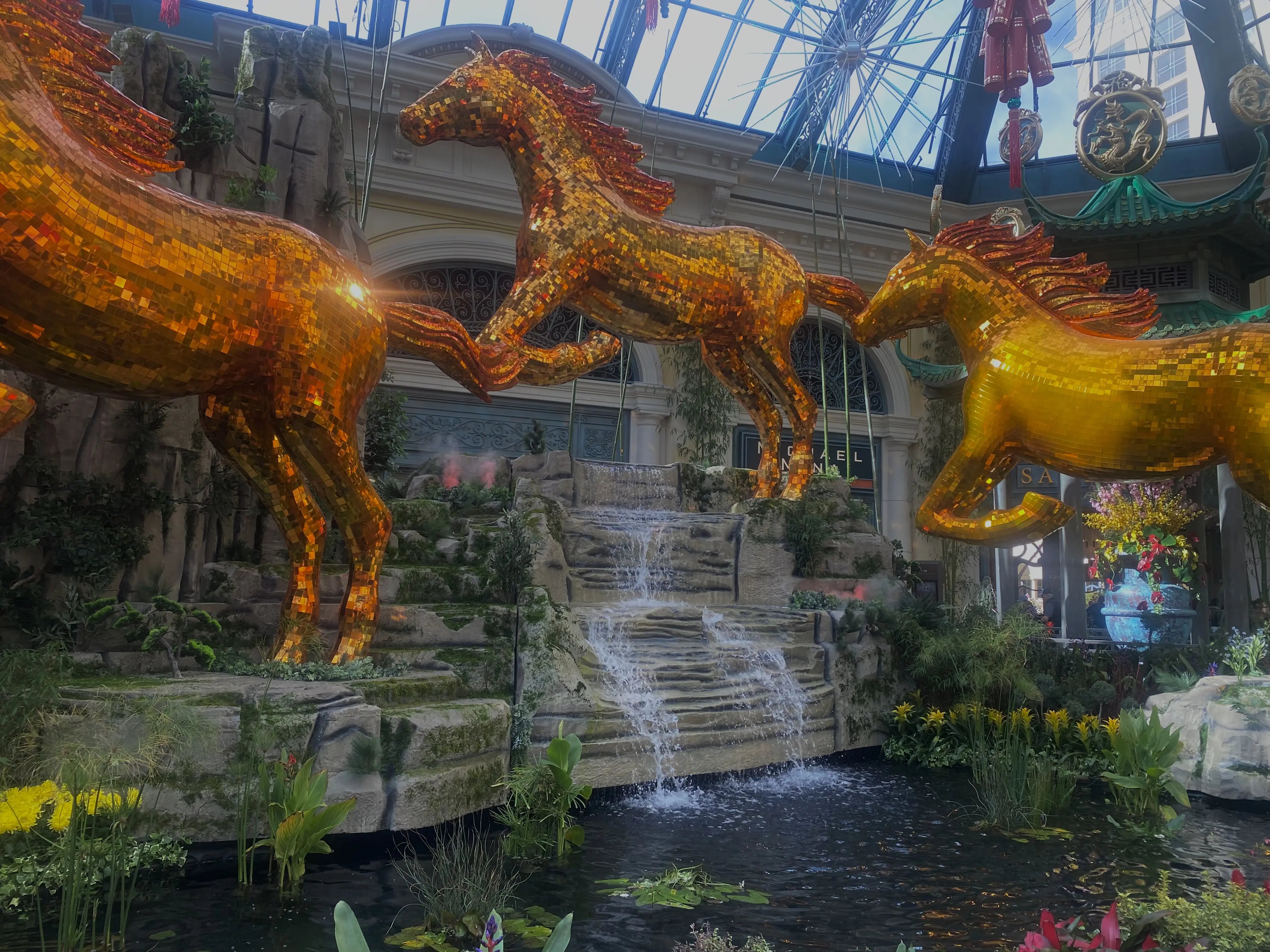 Three golden horses stand in front of a waterfall in the Bellagio's Conservatory West Bed